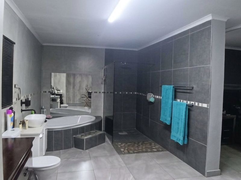 Modern open-plan bathroom featuring a walk-in shower, built-in bathtub, and contemporary grey tiling, seamlessly integrated with the adjacent bedroom area.