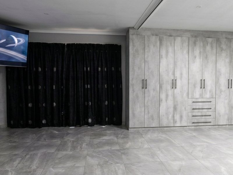 Spacious bedroom featuring extensive built-in cupboards with a modern grey finish and large format floor tiles.