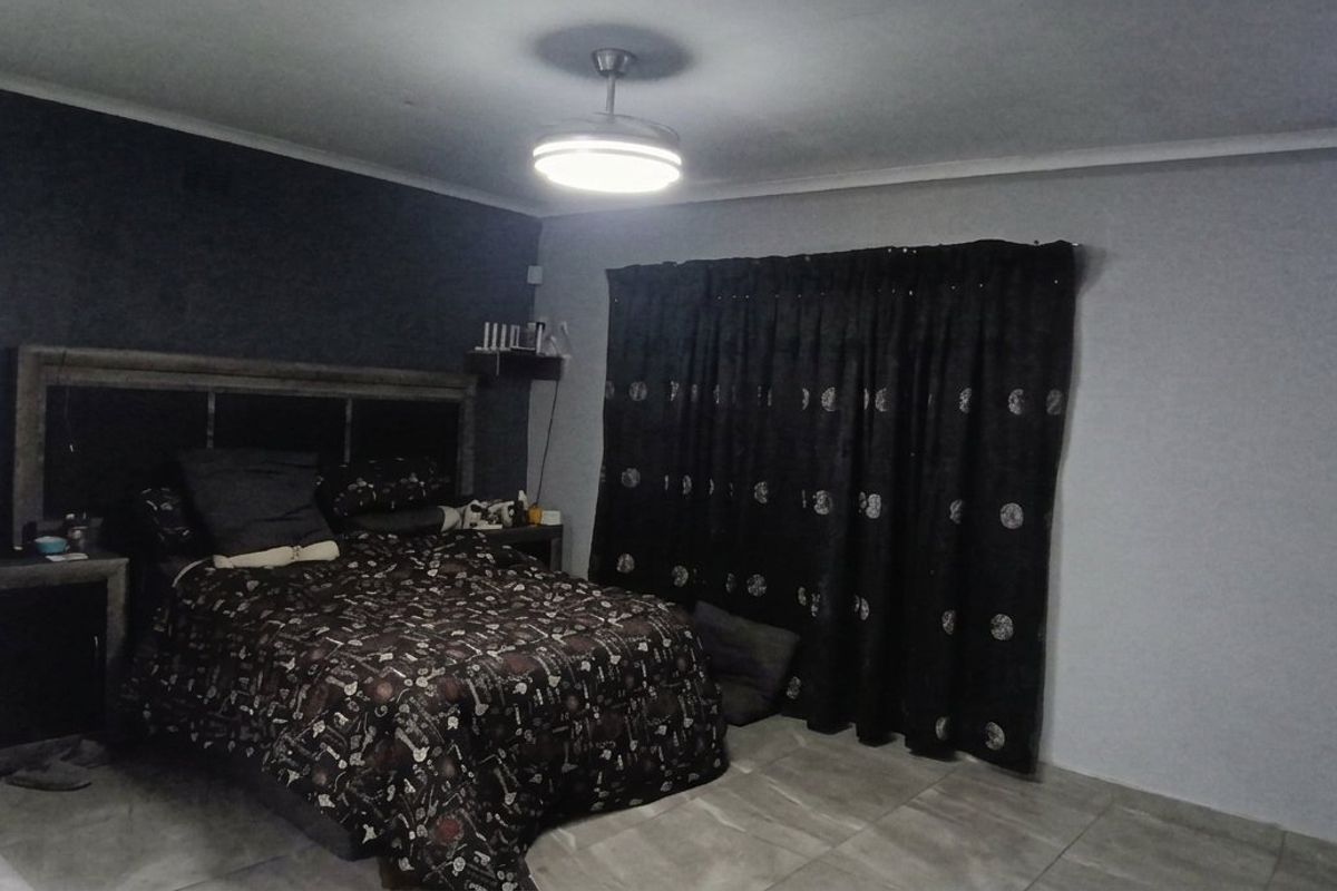 Spacious bedroom featuring tiled flooring, a central ceiling fan, and a dark accent wall, providing a functional and neutral sleeping space.