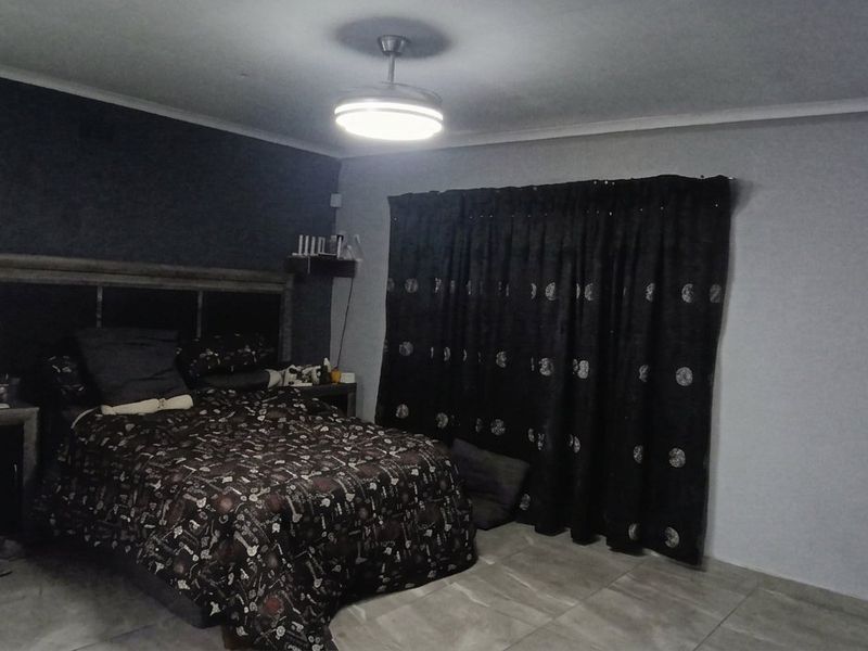 Spacious bedroom featuring tiled flooring, a central ceiling fan, and a dark accent wall, providing a functional and neutral sleeping space.