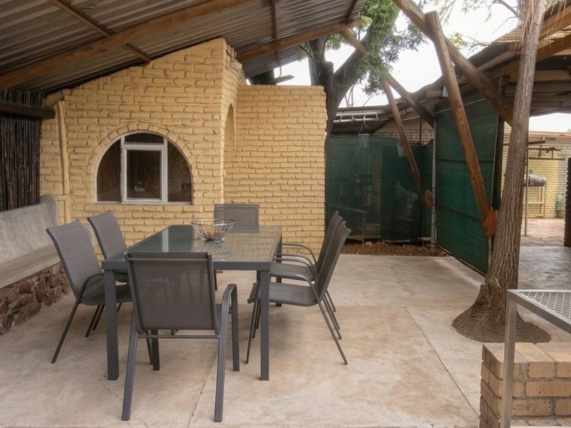 Covered outdoor patio area featuring a built-in concrete bench, stone masonry detailing, and a built-in braai, providing a rustic space for outdoor entertaining.