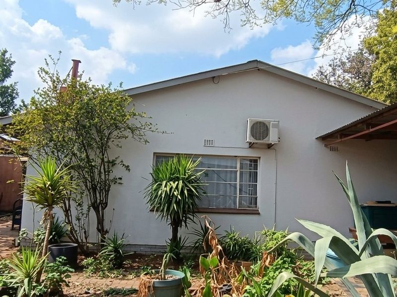 Rear view of the property showing the exterior wall, window, and an installed air conditioning unit with surrounding garden area.