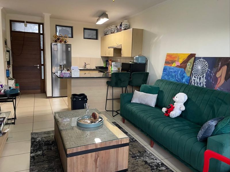 Open-plan living area featuring a compact kitchen with granite countertops, light wood cabinetry, and tiled flooring throughout the combined space.