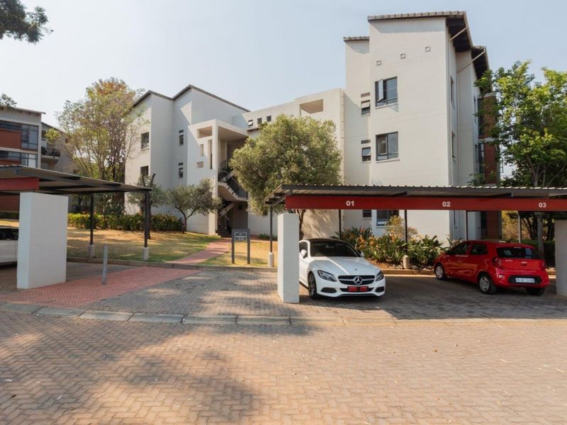 Exterior view of a multi-story residential complex featuring paved driveway access and designated covered parking bays for residents.