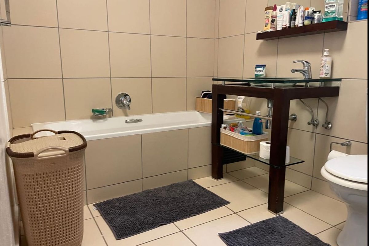 A functional bathroom featuring a built-in bathtub, vanity basin, and toilet with neutral ceramic wall and floor tiling.