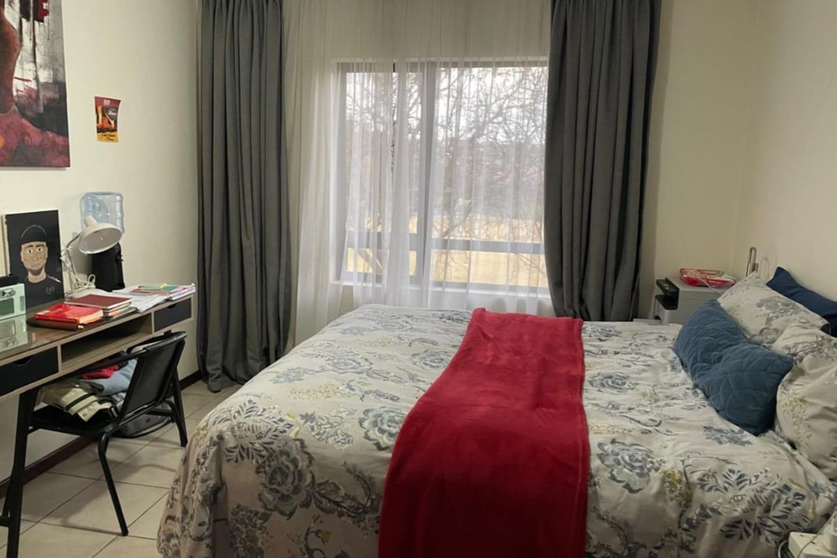 A functional bedroom featuring tiled flooring and a large window with curtain tracks, providing natural light and a view of the outdoors.