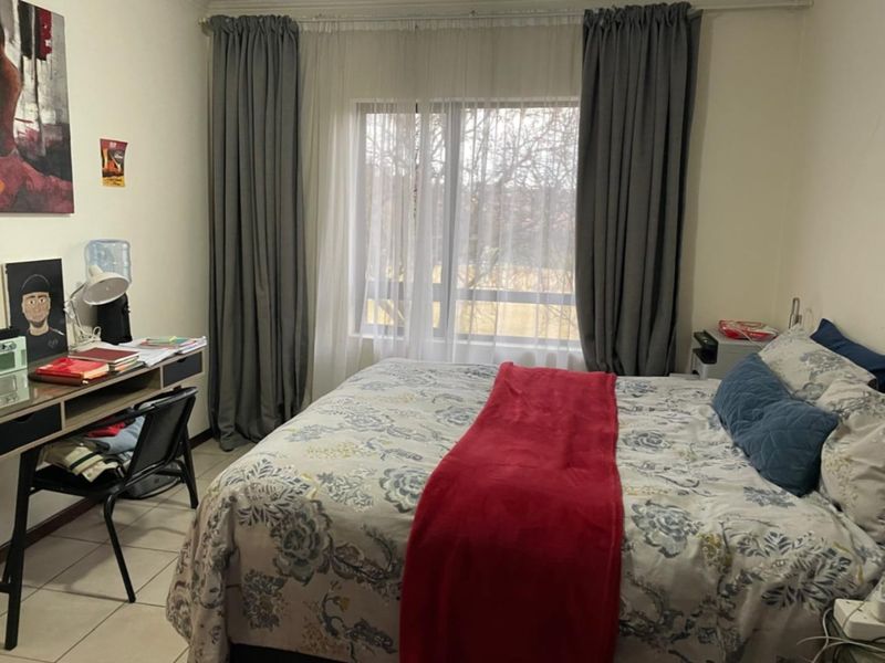 A functional bedroom featuring tiled flooring and a large window with curtain tracks, providing natural light and a view of the outdoors.