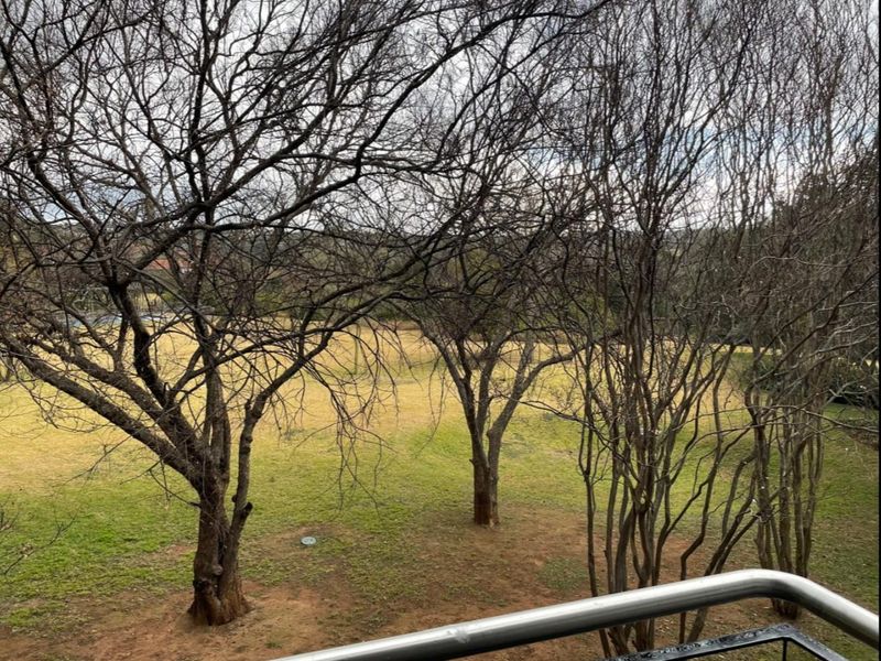 A view from a balcony overlooking a grassy area with mature trees.