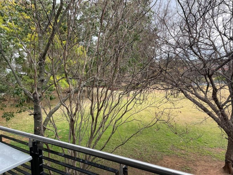 A view from a balcony overlooking a spacious garden area with mature trees and lawn.