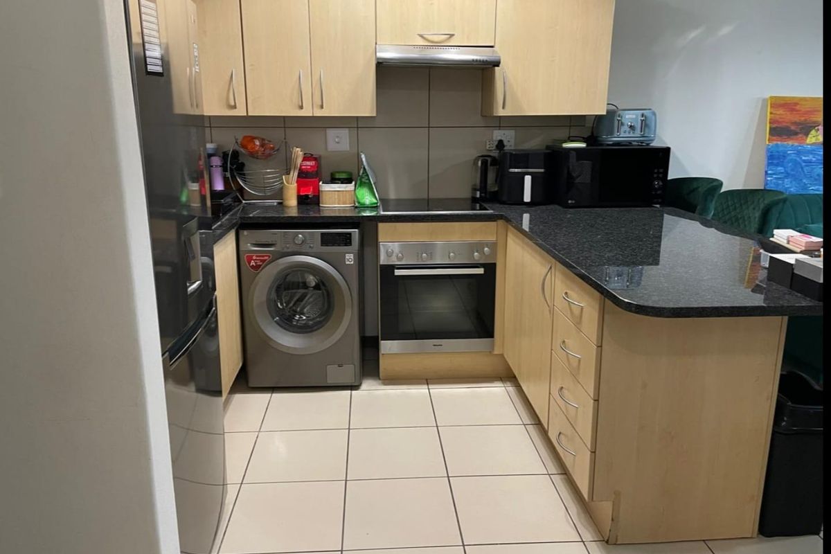 Compact kitchen featuring light wood cabinetry, granite countertops, built-in oven, hob, extractor fan, and tiled flooring with an integrated laundry appliance space.