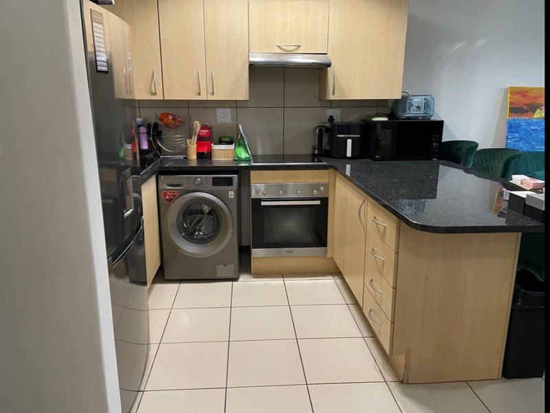 Compact kitchen featuring light wood cabinetry, granite countertops, built-in oven, hob, extractor fan, and tiled flooring with an integrated laundry appliance space.