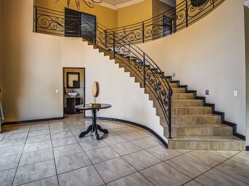 Grand entrance hall featuring a sweeping curved staircase with decorative wrought iron balustrades and neutral tiled flooring.
