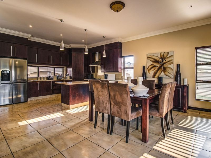 Spacious open-plan kitchen and dining area featuring dark wood cabinetry, stone countertops, a central island, and ceramic floor tiles throughout.
