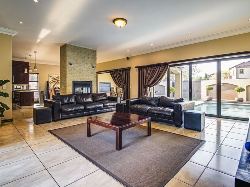 Spacious open-plan living area featuring a central stone-clad fireplace, tiled flooring, and large sliding doors providing seamless access to the outdoor pool area.