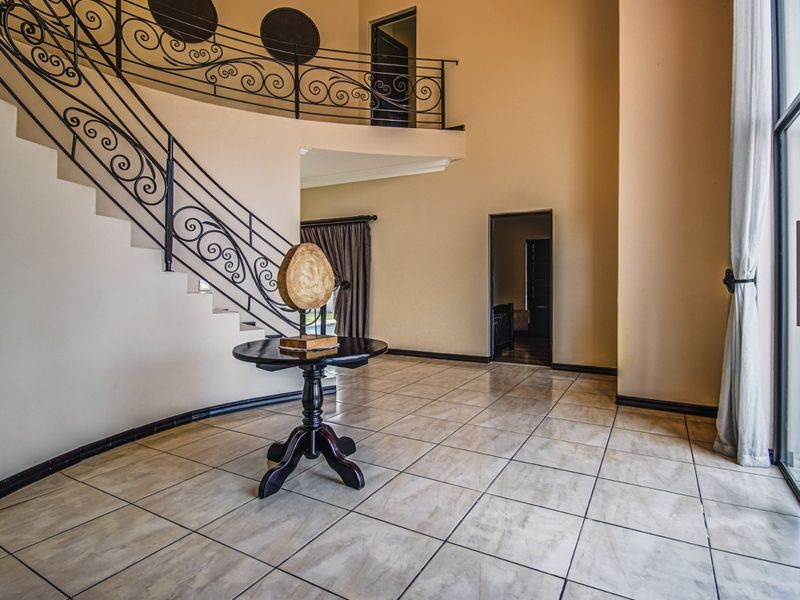 Spacious double-volume entrance hall featuring tiled flooring, a decorative wrought iron staircase, and large glass doors providing natural light.