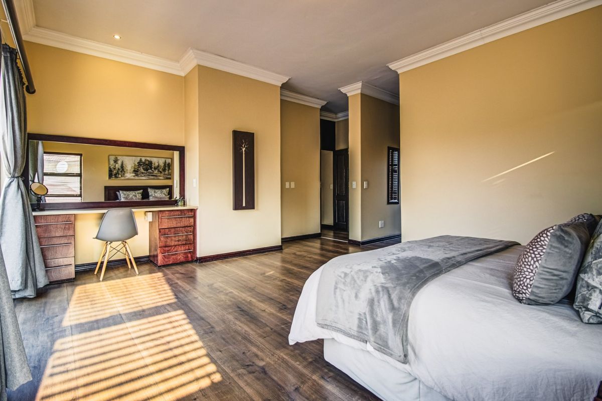 Spacious bedroom featuring warm-toned walls, dark laminate flooring, crown molding, and a built-in vanity area with a large mirror.