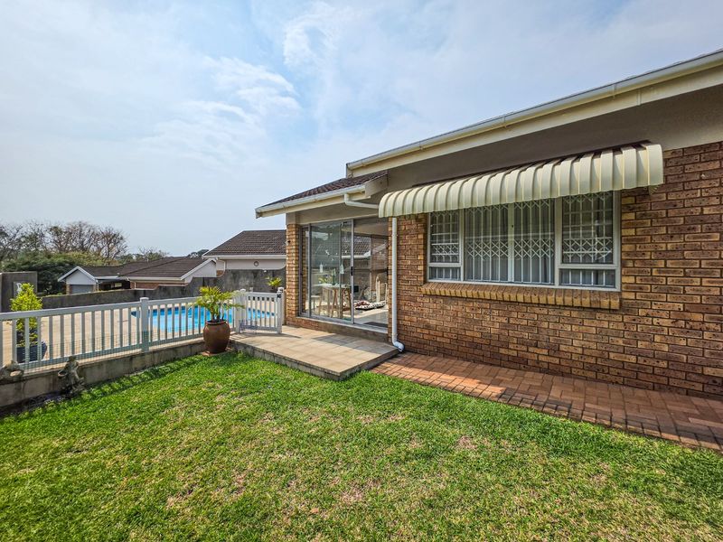 Rear view of the townhouse featuring a brick facade, paved patio area, lawn, and a private swimming pool with a white picket fence.