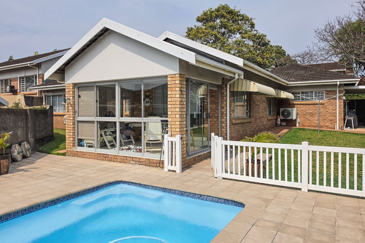 Rear view of the townhouse featuring a swimming pool, paved patio area, and an enclosed sunroom with brick exterior walls.