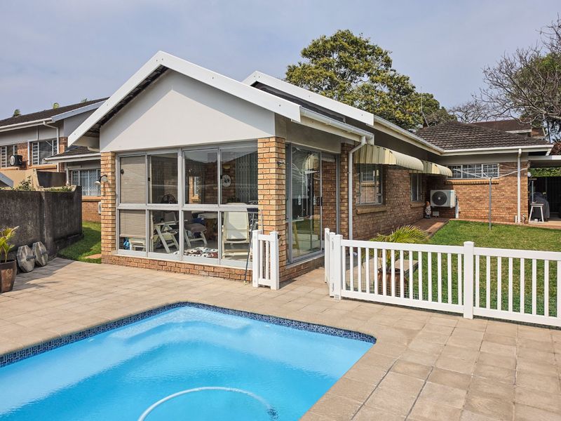 Rear view of the townhouse featuring a swimming pool, paved patio area, and an enclosed sunroom with brick exterior walls.