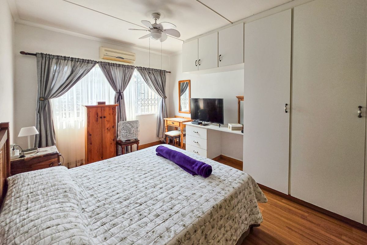 A well-lit bedroom featuring built-in cupboards, laminate flooring, a ceiling fan, and an air conditioning unit.