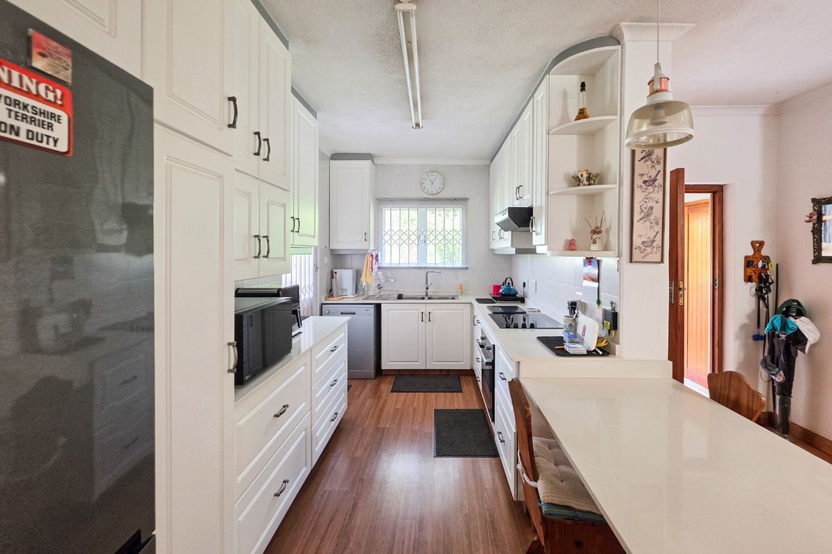A functional kitchen featuring white cabinetry, laminate flooring, a breakfast bar, and integrated appliances, offering a clean and practical workspace.