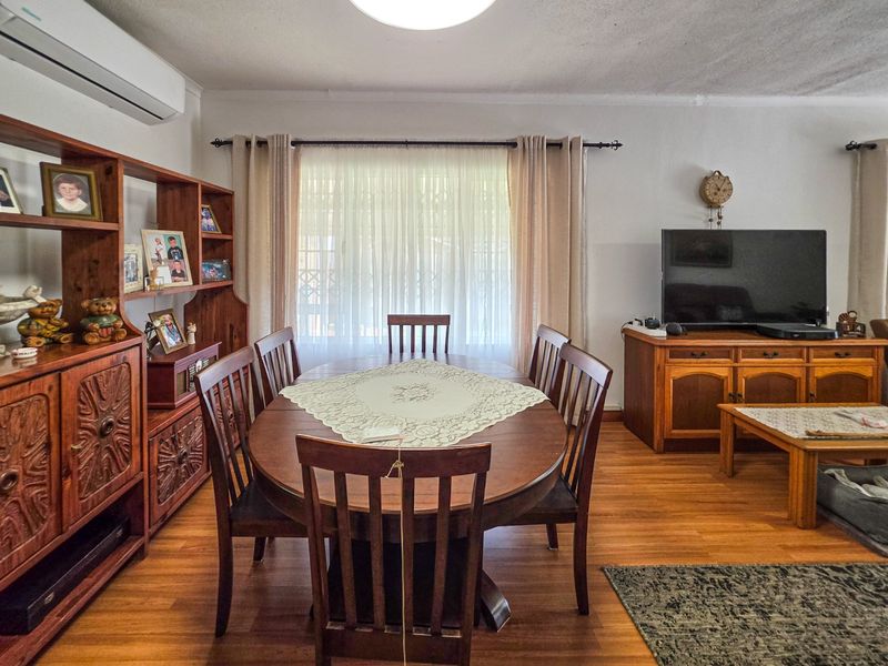 A living and dining area featuring laminate flooring, a wall-mounted air conditioning unit, and large windows with curtain treatments.