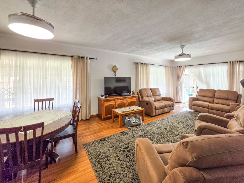 Spacious open-plan living and dining area featuring hardwood flooring, ceiling fans, and large windows providing ample natural light.