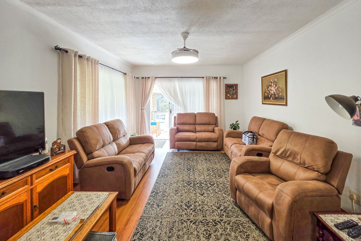 A comfortable living room featuring hardwood flooring, a central ceiling fan, and a sliding glass door providing access to the outdoor area.