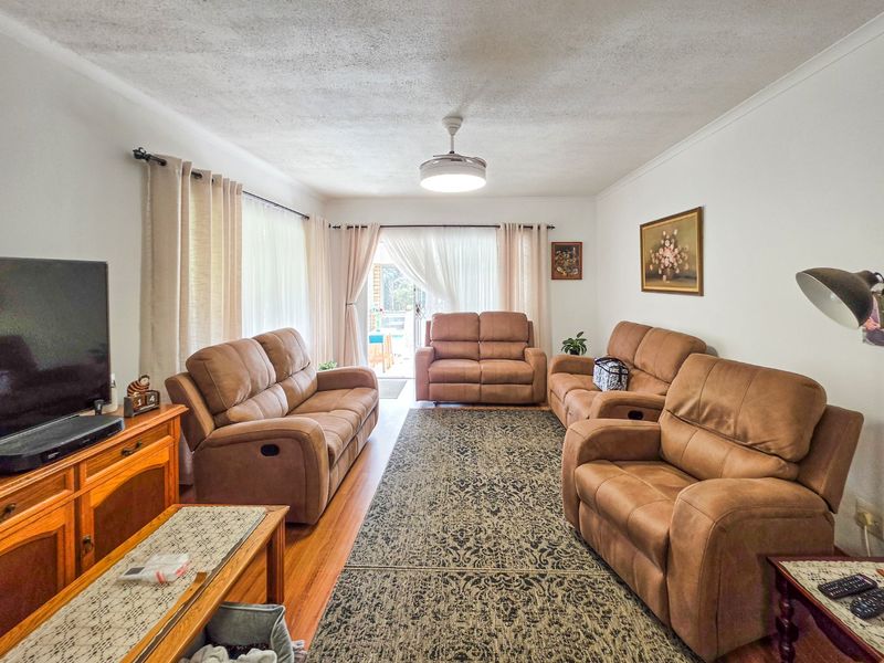 A comfortable living room featuring hardwood flooring, a central ceiling fan, and a sliding glass door providing access to the outdoor area.