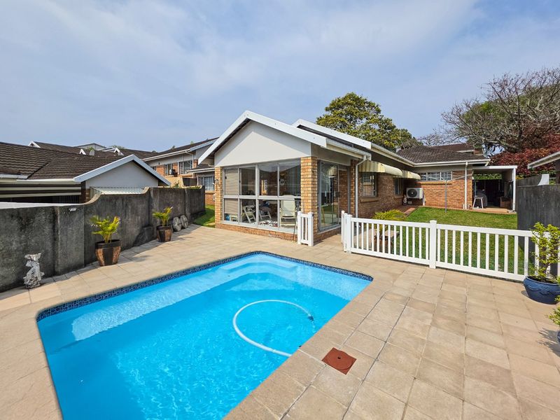 A private backyard featuring a swimming pool, paved patio area, and an enclosed sunroom, set within a secure townhouse garden with brick exterior finishes.