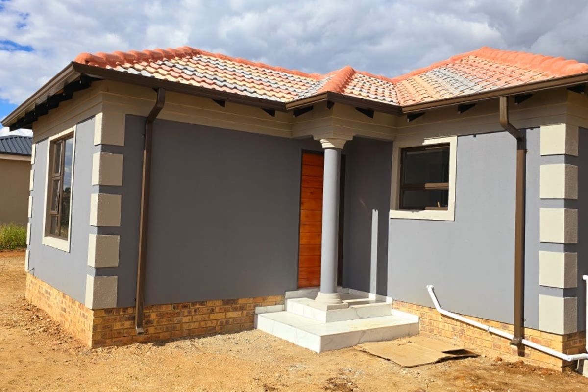 Front view of a modern single-story house featuring a terracotta tiled roof, grey rendered walls with corner detailing, and a covered entrance porch.
