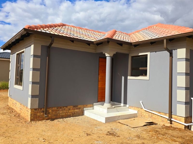 Front view of a modern single-story house featuring a terracotta tiled roof, grey rendered walls with corner detailing, and a covered entrance porch.