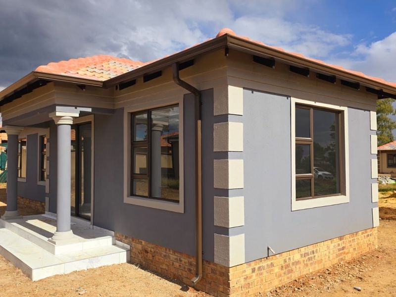 A modern single-story house exterior featuring grey rendered walls with contrasting quoins, terracotta roof tiles, and a covered entrance porch with concrete columns.
