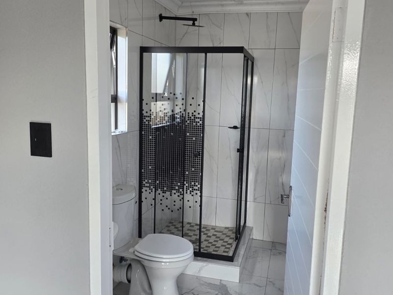 A modern, clean bathroom featuring a glass shower enclosure, white toilet, and contemporary marble-look wall and floor tiling.