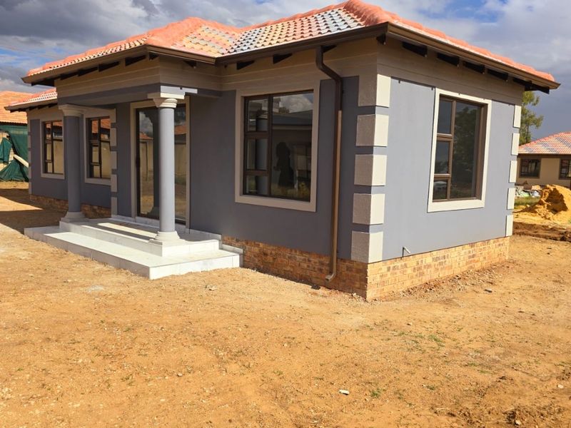 A newly constructed single-story house featuring a tiled roof, grey rendered walls with decorative quoins, aluminium window frames, and a covered entrance with concrete columns.