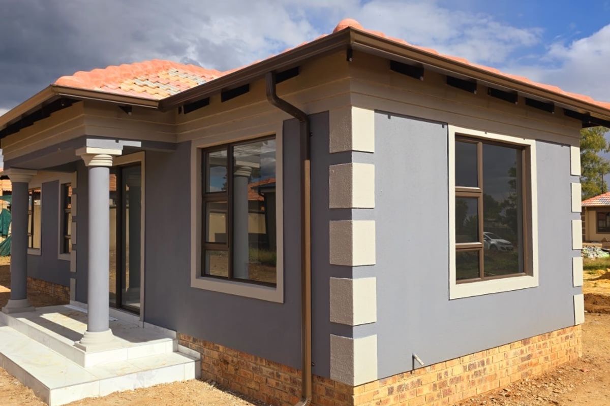 A modern single-story house exterior featuring grey rendered walls with contrasting quoins, terracotta roof tiles, and a covered entrance porch with concrete columns.