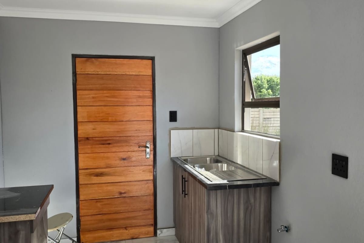 A compact kitchen area featuring modern marble-look floor tiles, wood-grain cabinetry, a stainless steel sink, and a solid timber door.