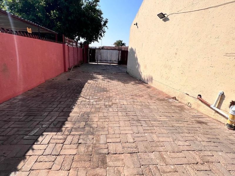 A paved driveway area featuring a perimeter wall, security gate, and exterior floodlight, with visible plumbing infrastructure along the side wall.