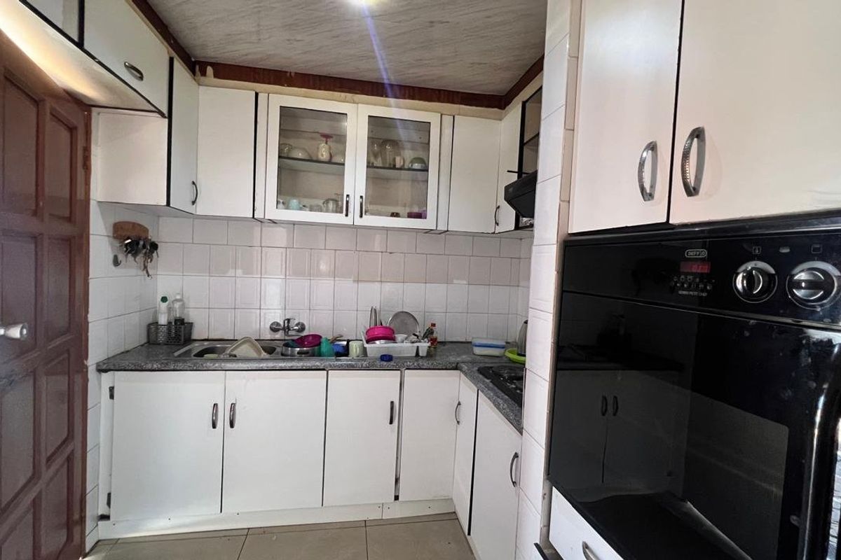 Compact kitchen featuring white built-in cabinetry, a tiled backsplash, stainless steel sink, and a built-in oven.