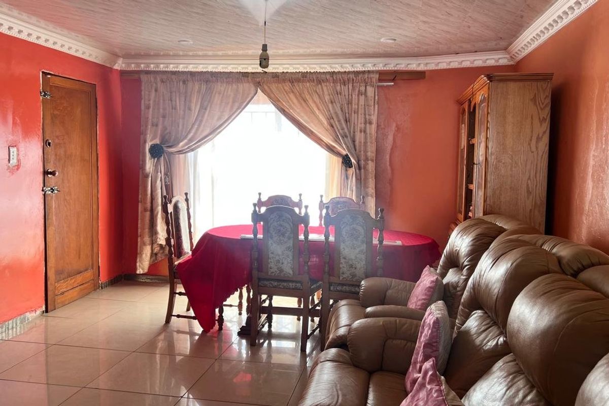 A living and dining area featuring tiled floors and decorative ceiling cornices, currently showing signs of wear on the wall surfaces.