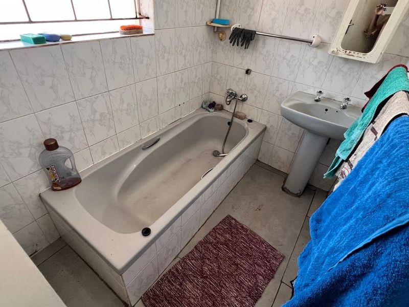 A dated bathroom featuring a standard bathtub, pedestal basin, and tiled finishes, requiring cosmetic updates to improve its overall condition and appeal.