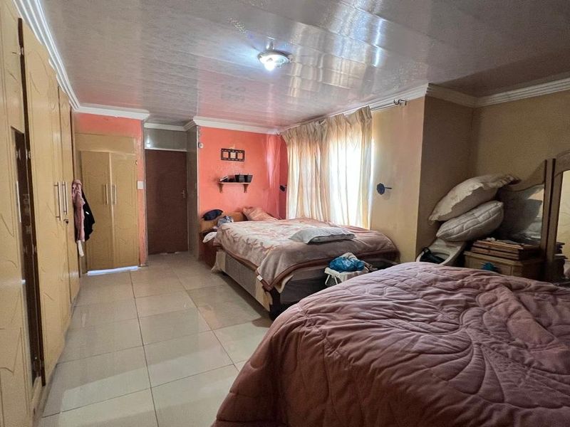 Spacious bedroom featuring built-in cupboards, tiled flooring, and ceiling cornice, offering a functional layout with potential for cosmetic updates.