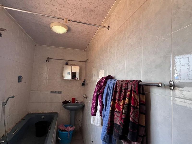 A functional bathroom featuring a pedestal basin, built-in bathtub, and full-height wall tiling, offering potential for modernization and cosmetic updates.