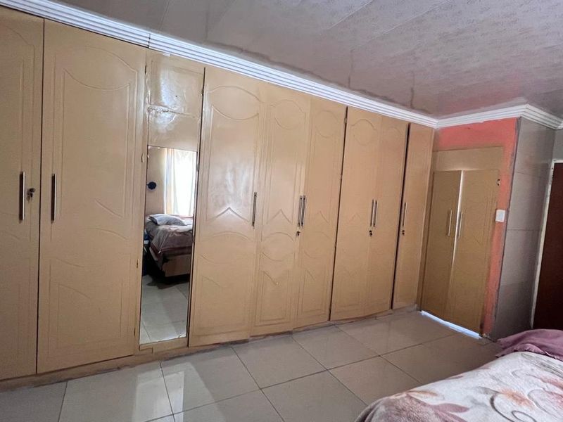 Bedroom featuring extensive built-in cupboards with a mirrored panel and tiled flooring throughout.