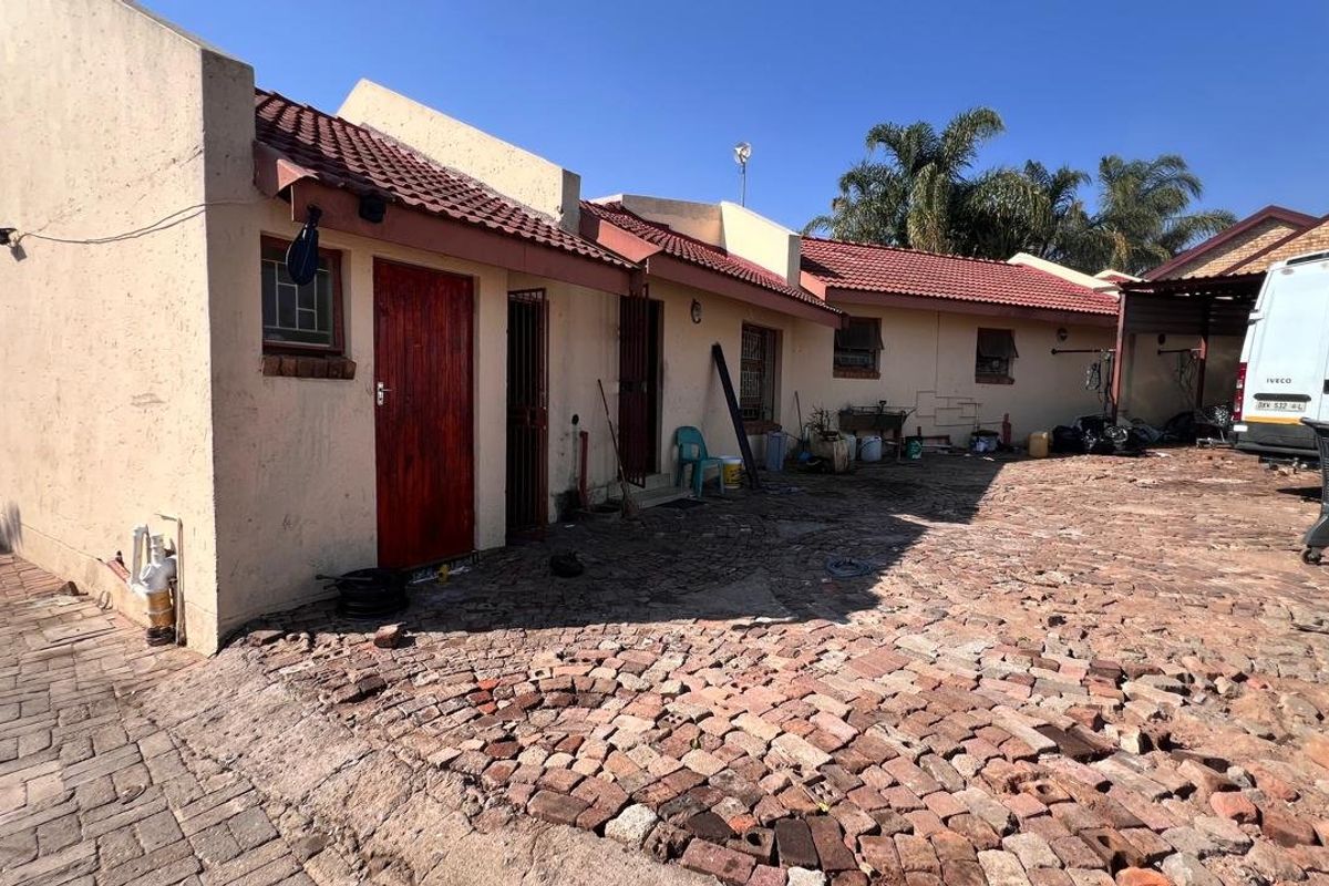 Rear exterior view of the property featuring a tiled roof, security gates, and extensive brick paving in need of maintenance.
