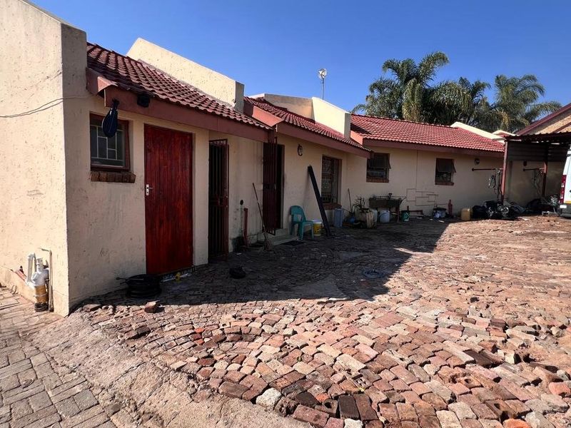Rear exterior view of the property featuring a tiled roof, security gates, and extensive brick paving in need of maintenance.