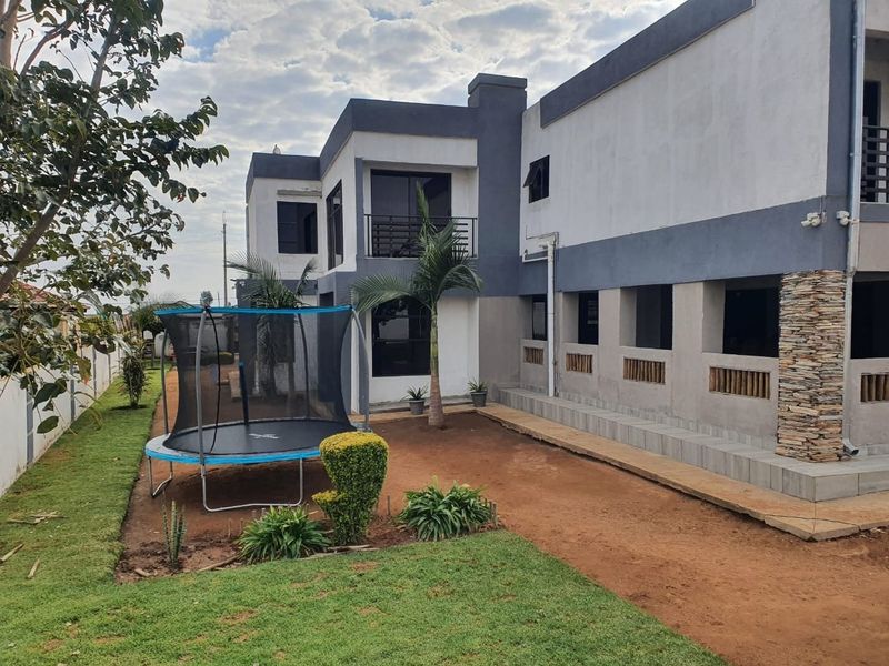 Rear view of a two-story house featuring stone cladding accents, a balcony, and a garden area with a paved walkway.