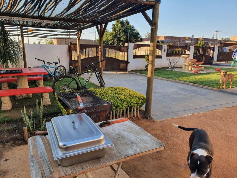 Outdoor entertainment area featuring a timber pergola, concrete driveway, perimeter wall with metal gates, and a landscaped garden with a water feature.