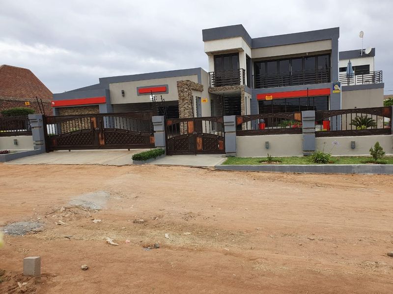 Modern double-storey residence featuring stone cladding, wrought iron perimeter fencing, automated gates, and a balcony, presenting a secure and contemporary street-facing facade.