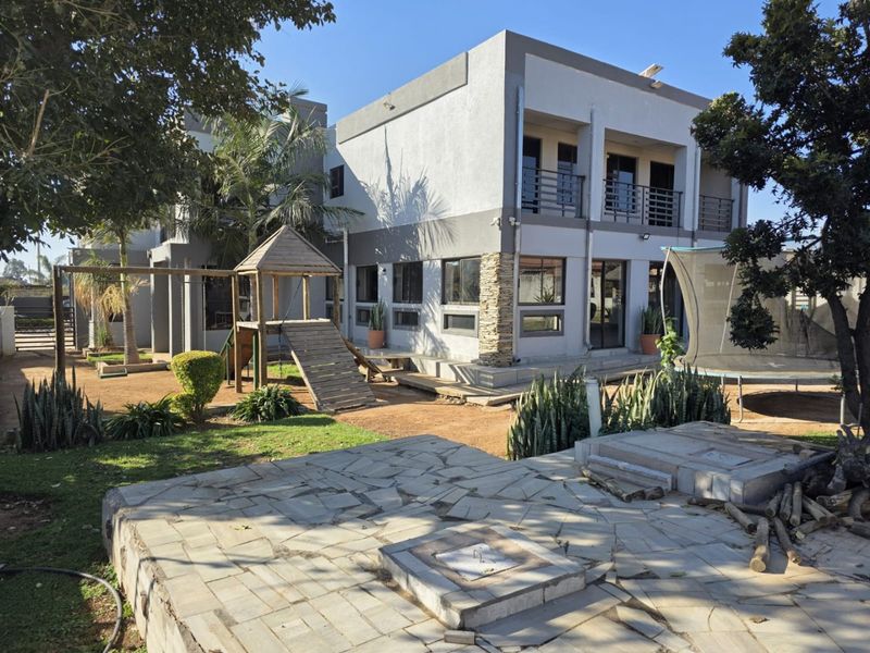 Rear view of a two-story house featuring a paved patio area, stone-clad pillar, and upper-level balconies with metal railings.